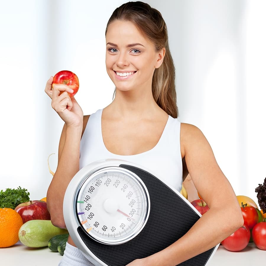 Woman holding a scale and an apple, ready to start her weight loss program